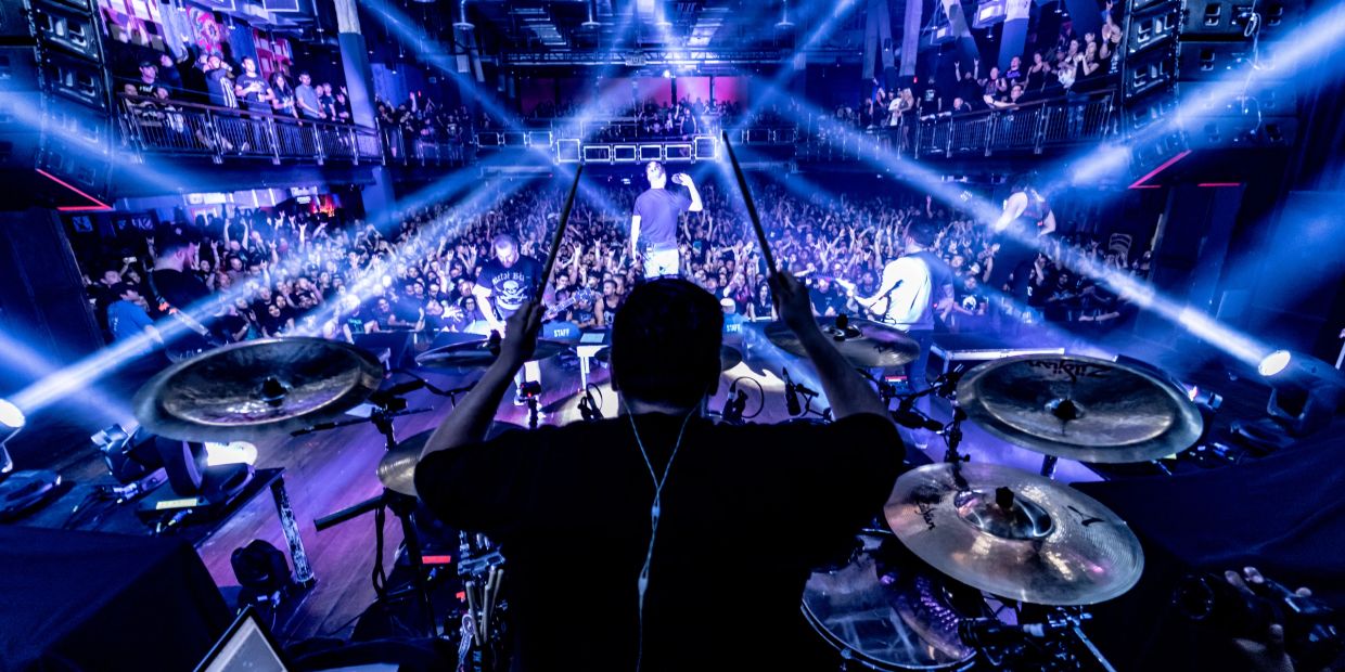 Drummer performing at a packed concert with vibrant lighting.