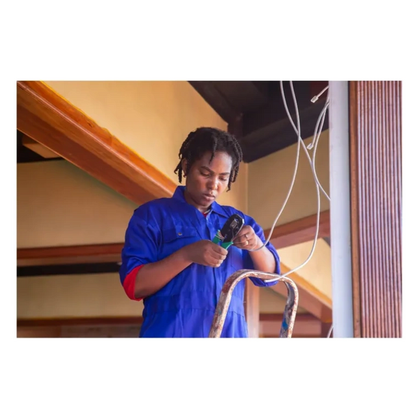 A woman electrician working on wiring indoors wearing a blue uniform.