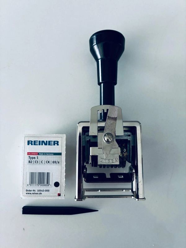 A metal numbering stamp with ink pad and black plastic tool on a white surface.