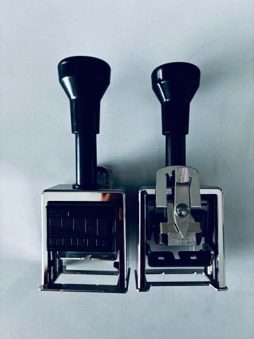Two black and silver date stamps on a white surface.