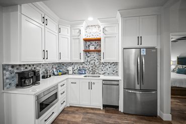 Modern white kitchen with stainless steel appliances and patterned backsplash.
