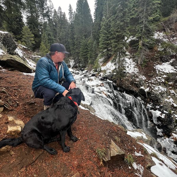 Man and black dog enjoying a snowy mountain waterfall.