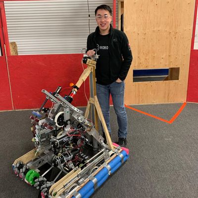 Person standing next to a complex robot inside an indoor arena.