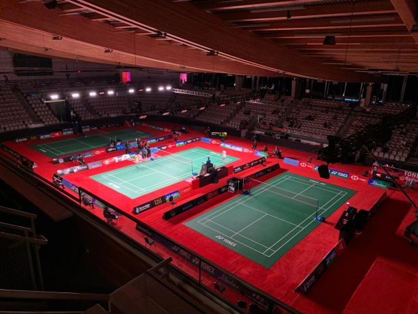 Indoor badminton courts with red flooring and seating area.