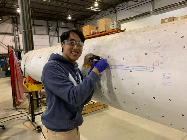 Person measuring large cylindrical object in industrial setting.
