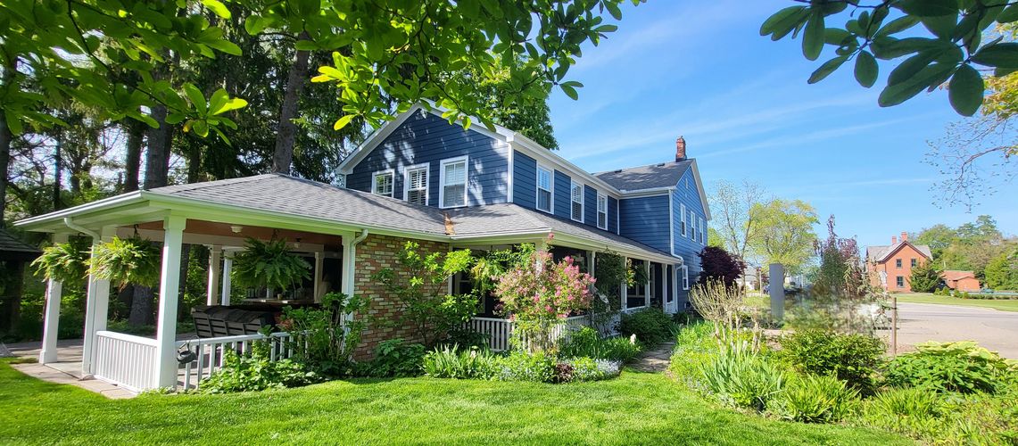 Blue two-story house with a garden and porch on a sunny day.