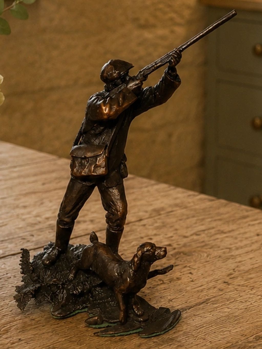 Bronze statue of a hunter aiming a rifle with his dog beside him.