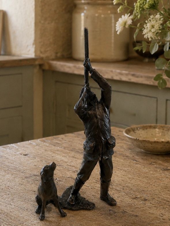 Bronze sculpture of a hunter aiming a rifle with a dog sitting beside him.