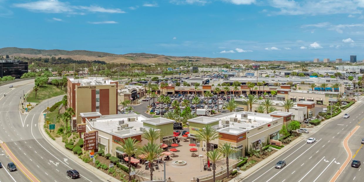 Aerial view of a suburban shopping center with parking and nearby roads.