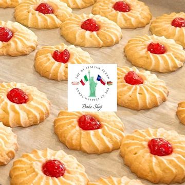 Golden cookies topped with red cherry preserves on parchment paper.