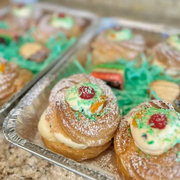 Delicious cream-filled pastries topped with icing and colorful sprinkles in a tray.