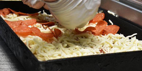 A deep dish pizza being topped with pepperonis before heading into the oven