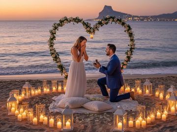 A romantic beach proposal at sunset with candles and heart-shaped floral arch.