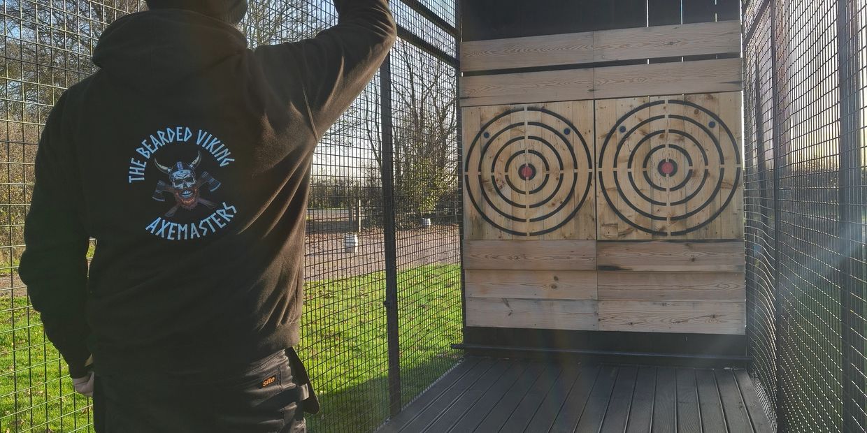 Person practicing axe throwing at an outdoor range with wooden targets.