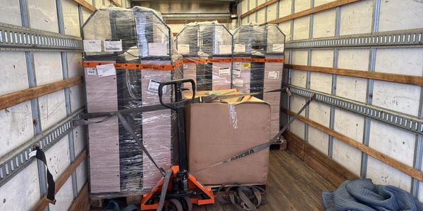 Packed truck interior with wrapped pallets and a pallet jack secured by straps.