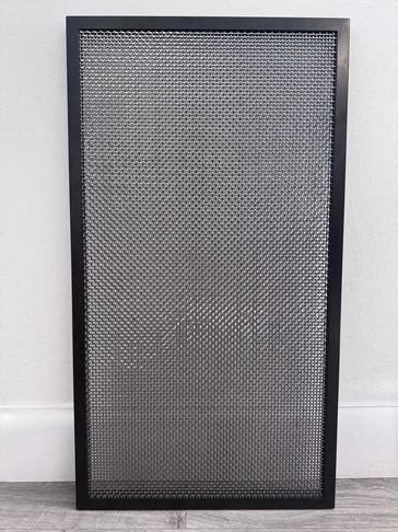 Black metal mesh panel with a rectangular frame leaning against a white wall.