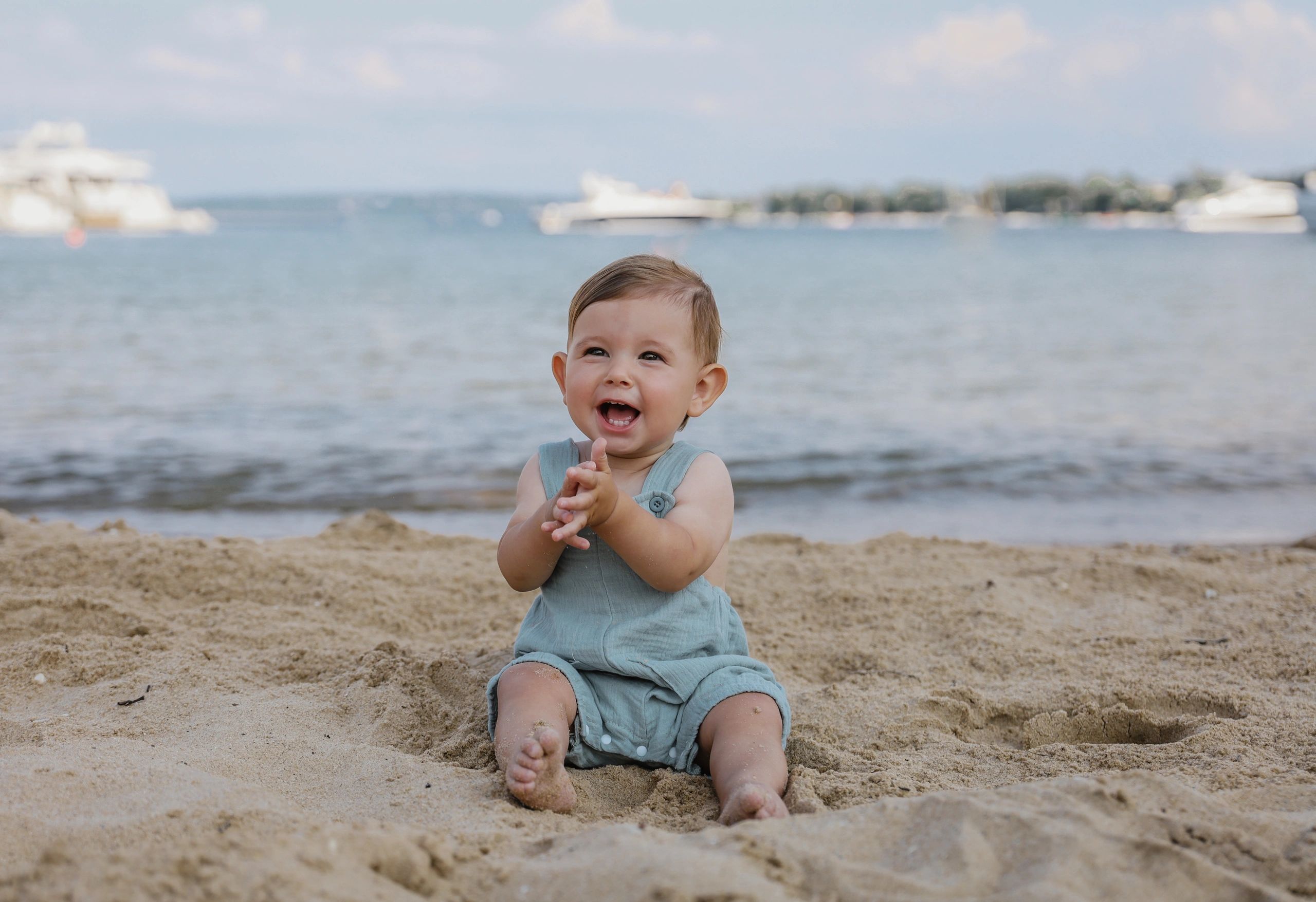 Happy baby clapping hands on a sandy beach near water.