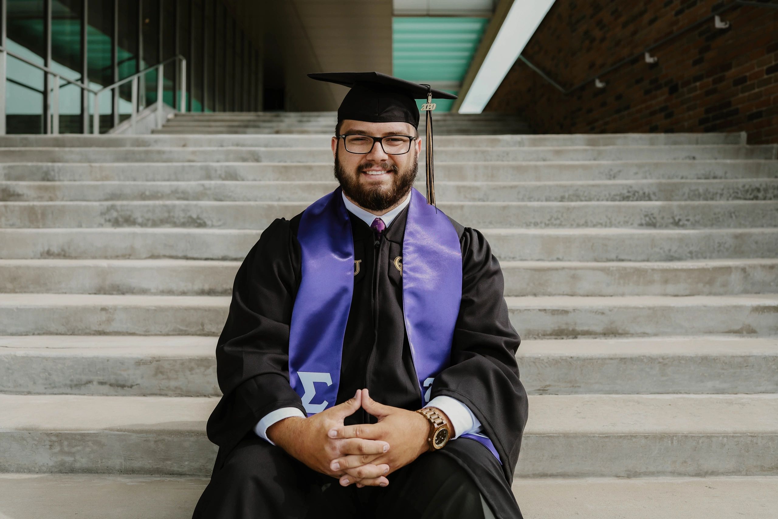 Graduate in cap and gown smiling on steps.