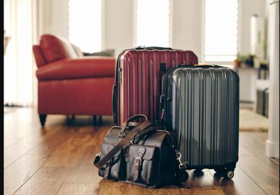 Two suitcases and a leather bag on a wooden floor in a living room.
