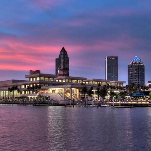 City skyline at sunset with waterfront and illuminated buildings.