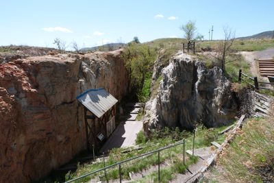 Rocky canyon entrance with wooden walkway and railing under clear sky.