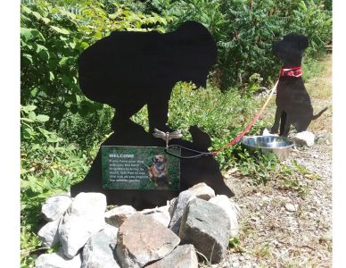 Black dog statues with a leash and dog bowl outdoors.