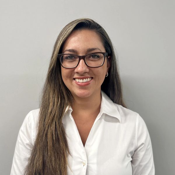 Woman with long hair and glasses smiles in white shirt.