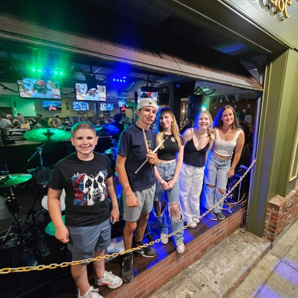 Group of five smiling teens posing in a music stage area.