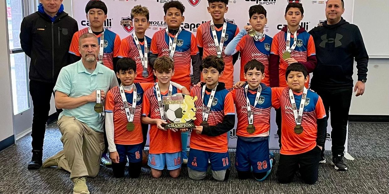 Youth soccer team posing with medals and championship trophy indoors.