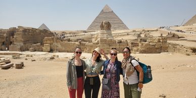 Four tourists posing in front of the Great Sphinx and pyramids in Egypt.