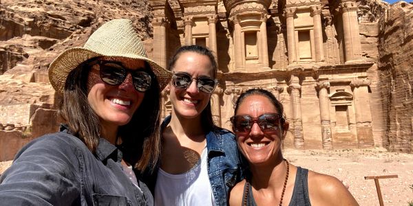 Three women smiling in front of the ancient Petra monument in Jordan.