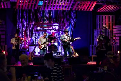 A band performs live on stage with vibrant purple lighting.