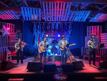 Band performing live on a colorful stage with guitars and violin.