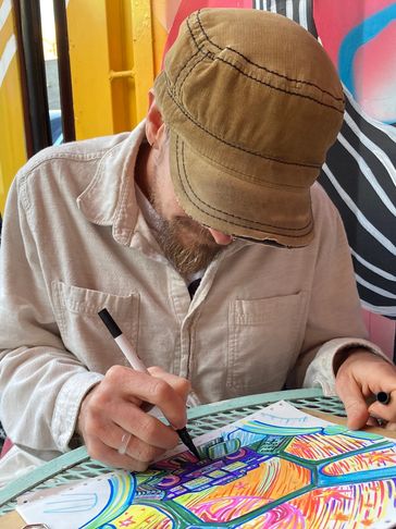 A man in a brown cap drawing colorful art at a table.