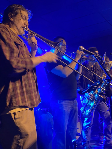 Three musicians passionately playing brass instruments on a dimly lit stage.