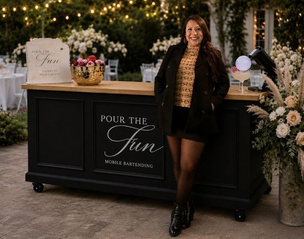 Woman standing beside a mobile bartending setup at an outdoor event.