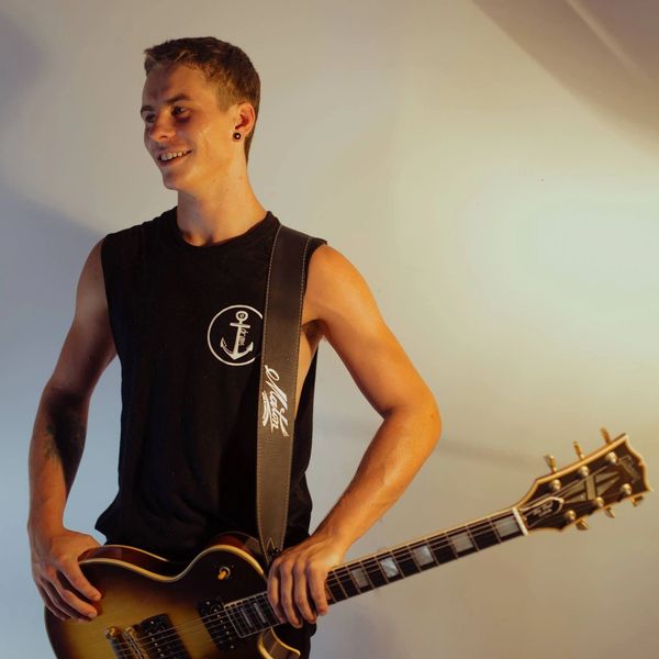 Young man smiling with electric guitar in a sleeveless black shirt.