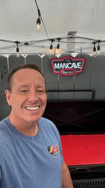 Man smiling inside a well-lit mancave with a neon sign.