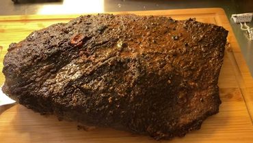 A large, seasoned smoked brisket on a wooden cutting board.