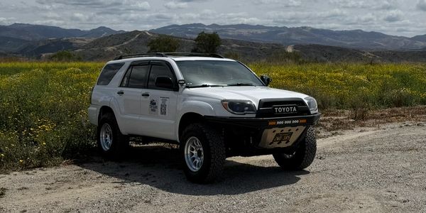 White Toyota SUV parked on a dirt road near wildflowers.