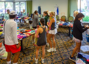 People browsing tennis apparel and accessories at an indoor sale event.