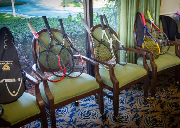 Tennis rackets resting on chairs in a cozy room with patterned carpet.