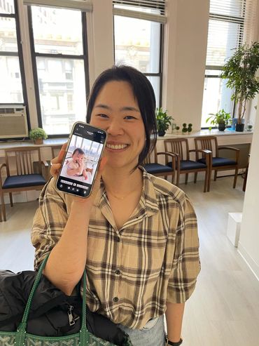Smiling woman showing a photo of a baby on her phone indoors.