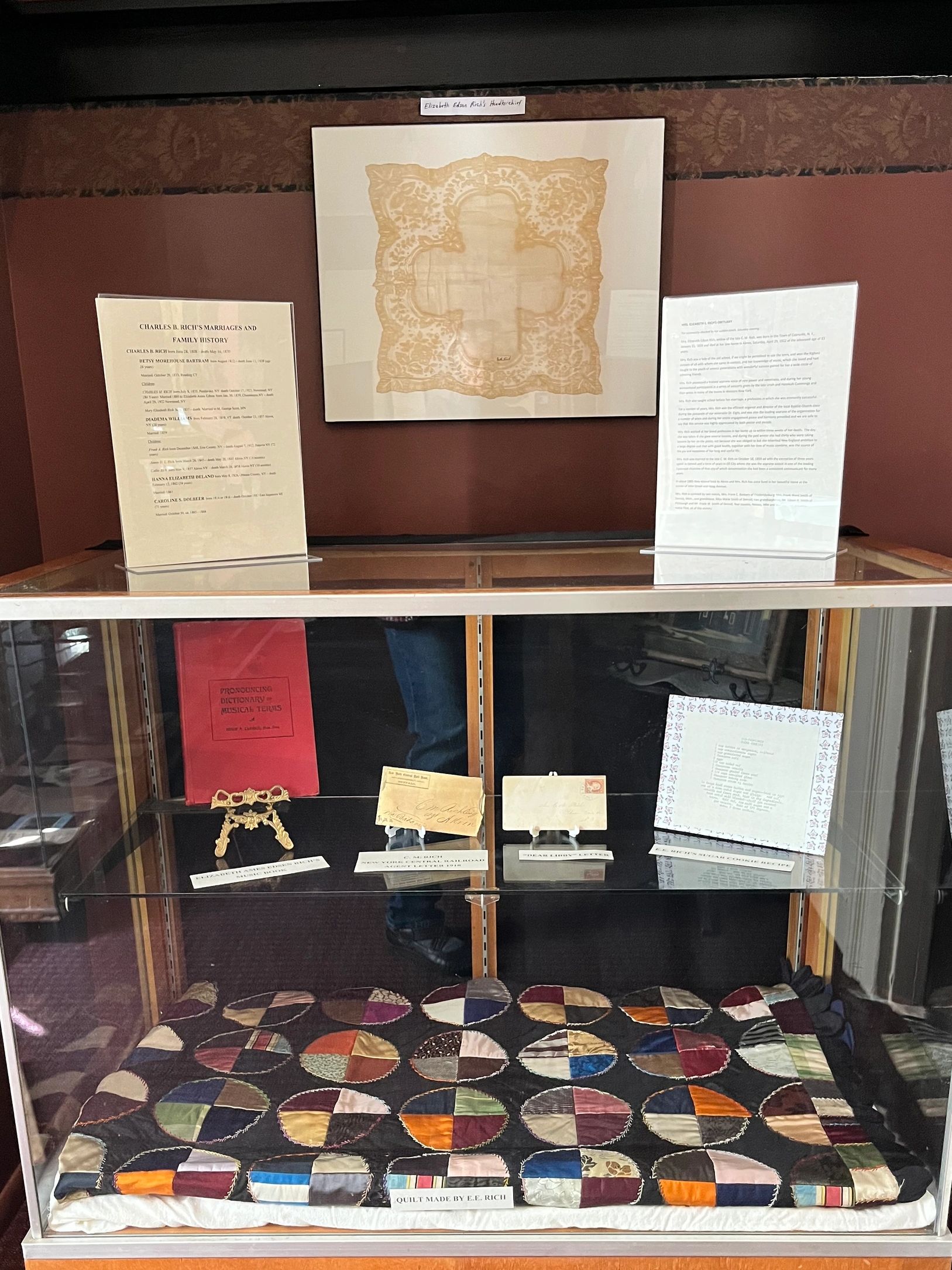 Museum display of an antique crazy quilt and an antique lace-trimmed lady's handkerchief.  