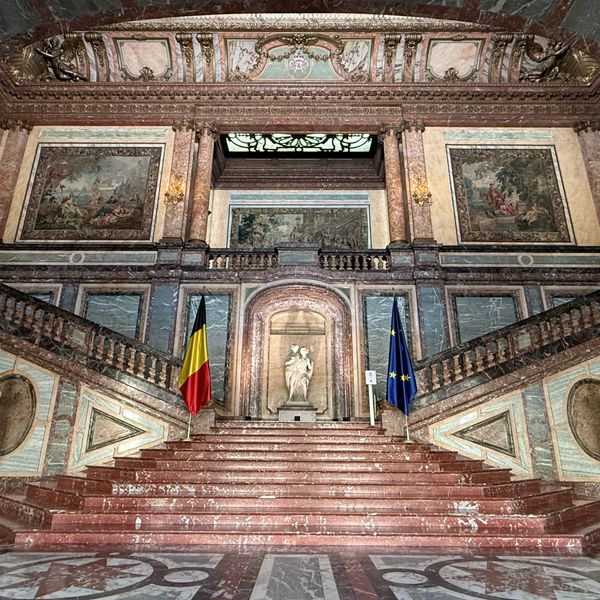Grand marble staircase with Belgian and EU flags and classical art.