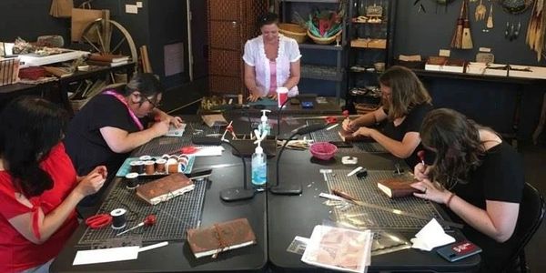 A group of people sitting around a table, being led in a crafting session making leather-bound journ