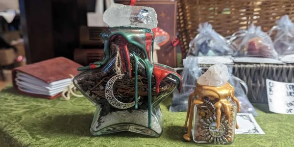 Two small spell jars, one shaped like a star and one square-shaped, sealed with colorful wax and ado