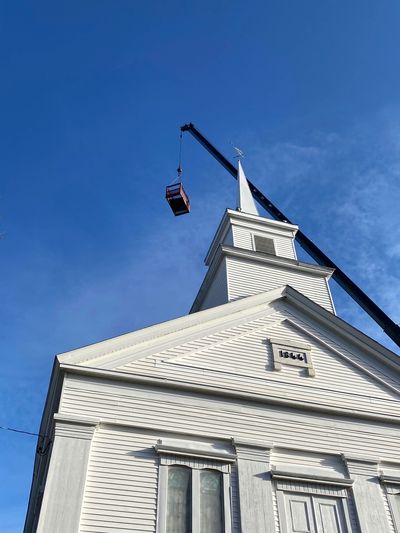 Crane lifting a church bell tower against a clear blue sky.