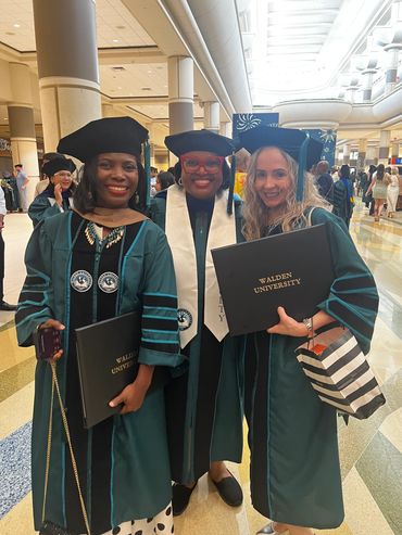 Three graduates in caps and gowns proudly holding Walden University diplomas.