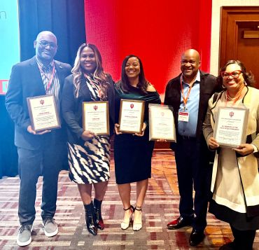 Five individuals proudly holding awards at a formal event.